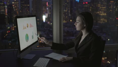 Good-Looking-Woman-Working-with-a-Computer,-Ballpoint-Pen,-Pad-and-a-Phone-in-Multistory-Office-Building.-Calling-Colleagues,-Big-City-Can-Be-Seen-through-Window.