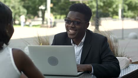 African-man-explaining-business-strategy-to-his-african-female-colleague,-using-laptop-during-meeting-at-a-cafe