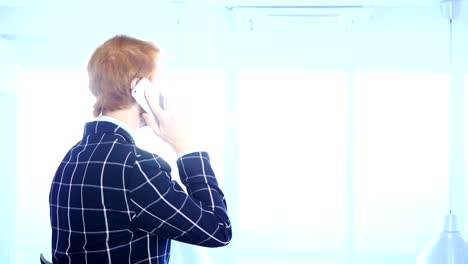 Redhead-Businessman-Talking-on-Phone,-Looking-through-Window,-Back-View