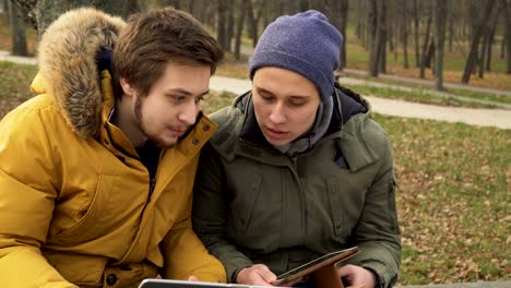 Two-friends-students-uses-laptop-and-tablet-outdoors