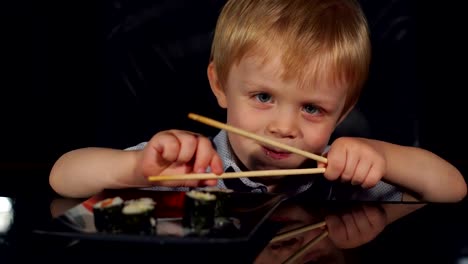 Cute-little-boy-eat-sushi-with-wooden-chopsticks.