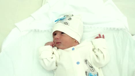 Close-up-of-newborn-baby-in-white-hat-lies-on-bed.