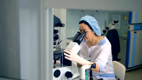 A-woman-in-scrubs-uses-one-of-laboratory-microscopes.