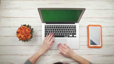 Frau-freier-fügt-ein-Kopfhörer-in-einen-Laptop,-stehend-auf-dem-weißen-Holztisch-mit-Blumen-und-orange-Tablette,-und-arbeitet-darauf.-Ansicht-von-oben.-Hände-hautnah