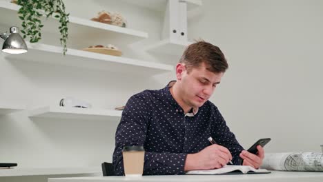 A-Young-Man-Writing-and-Using-a-Phone-Indoors