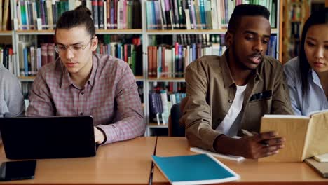 Bandeja-de-tiro-de-los-estudiantes-de-la-etnia-concentrado-Multi-hablando-y-preparando-para-el-examen-mientras-estaba-sentado-en-la-mesa-en-la-biblioteca-de-la-Universidad