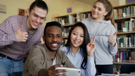 Gruppe-von-internationalen-Studenten-Spaß-haben,-lächelnd-und-Selfie-Fotos-auf-Smartphone-Kamera-an-der-Universitätsbibliothek.-Fröhliche-Freunde-haben-Pause,-während-Preapre-Projekt-zusammen