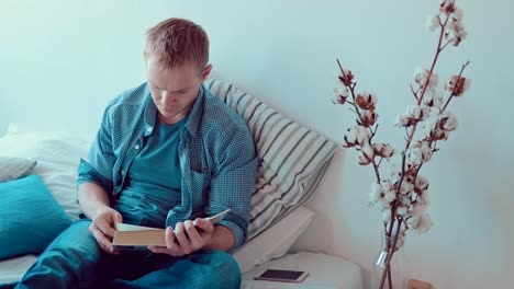 Young-man-reading-book-siting-on-the-sofa-in-home.-Indoor