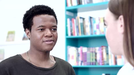 Close-up-of-handsome-African-American-young-man-talking-to-his-female-fellow-student-in-college-library.