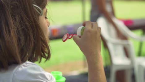 Niña-joven-con-pompas-de-jabón-fuera-en-el-campamento-de-verano-en-cámara-lenta-de-campo-verde