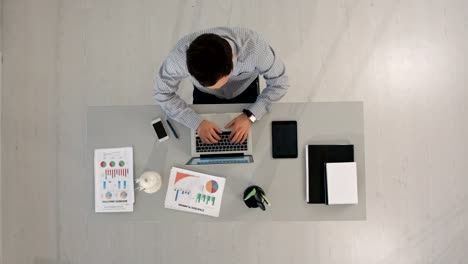 Hombre-trabajando-en-su-computadora-portátil-escribiendo-en-computadora-sentado-en-la-mesa.-Vista-superior