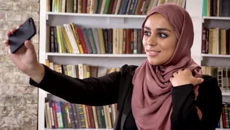 Portrait-of-young-muslim-pretty-women-in-hijab-taking-selfie-then-looking-at-phone-and-watching-photos-in-library,-smiling