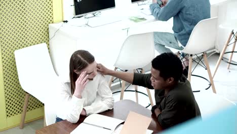 Vista-de-ángulo-alto-de-estudiantes-africanos-consolando-a-su-novia-exhausta-y-frustrada,-teniendo-problemas-con-el-estudio.-Niño-sentado-en-el-escritorio,-manteniendo-la-mano-en-su-hombro-y-diciendo-palabras-alentadoras