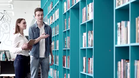 Hombre-joven-y-mujer-junto-a-shelevs-en-la-biblioteca-y-elegir-libros.-Hombre-contando-sobre-sus-libros-favoritos-a-novia