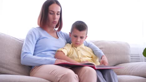 Mother-sitting-on-couch-and-reading-book-with-son