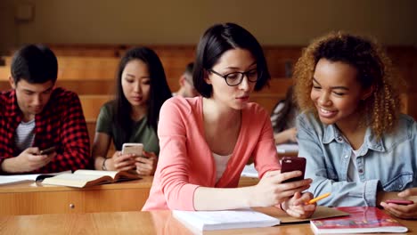 Hübsche-Mädchen-Studenten-nutzen-Smartphone,-Bildschirm,-beobachten,-redeten-und-lachten-sitzen-am-Schreibtisch,-an-der-Universität.-Social-Media,-Internet,-Millennials-und-Bildung-Konzept.