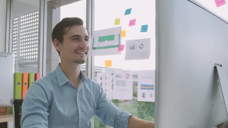 Young-caucasian-businessman-looking-at-the-monitor-of-a-personal-computer-and-smiles,-working-in-a-home-office