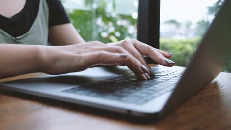 A-woman's-hands-working-and-typing-on-laptop-keyboard-on-wooden-table