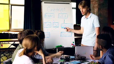 Kreative-Manager-nutzt-Whiteboard-an-Business-meeting-auf-Chart-zeigen-und-reden,-während-die-Gruppe-von-Menschen-ist-zuhören-und-Lernen-neuen-Informationen.