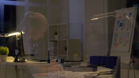 glass-wall-reflection-of-woman-with-working-at-night-office