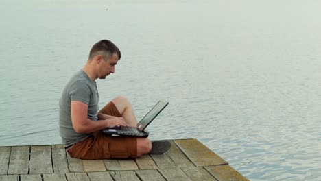 Vista-lateral-completo-de-sonriente-hombre-maduro-usando-laptop-en-muelle