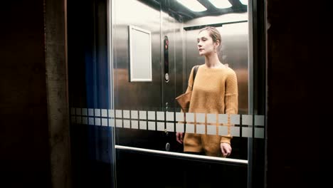 Young-confident-European-woman-pushes-elevator-button,-door-closes-and-she-rides-down,-view-through-a-glass-wall