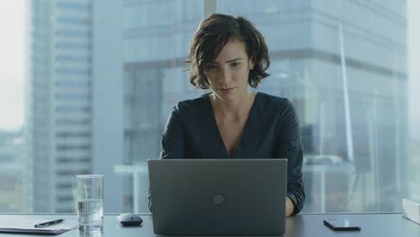 Beautiful-Successful-Female-CEO-Works-on-a-Laptop-in-Her-Modern-Sunny-Office-with-Cityscape-Window-View.-Strong-Female-Business-Leader.