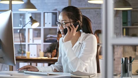 Asian-Female-Manager-Talking-on-Phone-and-Working-on-Computer