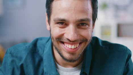 Portrait-of-Handsome-Man-Sitting-at-Desk-in-His-Living-Room-and-Charmingly-Smiling.