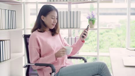 Beautiful-smart-business-Asian-woman-in-smart-casual-wear-using-smartphone-and-drinking-warm-cup-of-coffee-while-sitting-on-table-in-creative-office.-Lifestyle-women-working-at-office-concept.