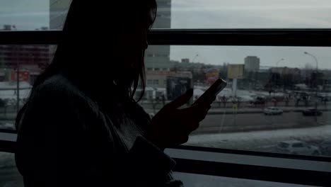 Chica-joven-en-un-suéter-gris-con-un-teléfono-en-un-café-por-la-ventana-en-el-fondo-de-la-megalópolis.