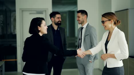 Pretty-young-woman-is-getting-job-in-successful-company-shaking-hands-with-CEO-and-smiling-while-other-workers-are-clapping-hands-and-expressing-positive-emotions.