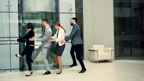 Playful-coworkers-are-enjoying-party-at-work-dancing-in-lobby-together-relaxing-and-laughing-wearing-suits.-Informal-communication,-happiness-and-team-concept.