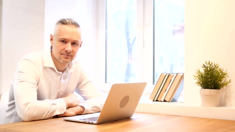 Middle-Age-Man-Looking-Toward-Camera-while-Working-on-Laptop