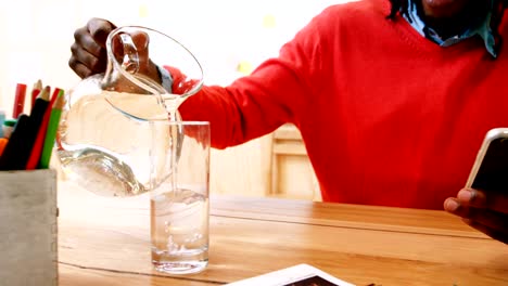 Man-pouring-jug-of-water-in-glass-while-using-mobile-phone
