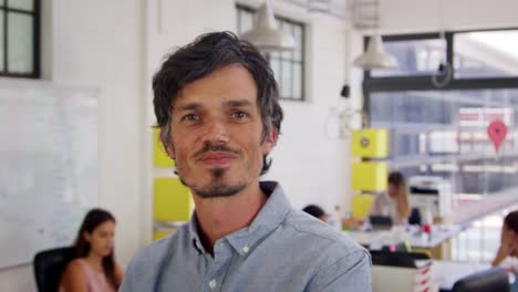 Mid-adult-white-man-in-office-walks-into-focus-and-smiles