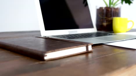 Laptop,-notebook-and-cup-of-coffee-arranged-on-wooden-table