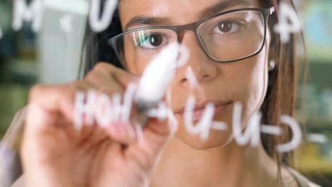 Junge-attraktive-Büroangestellte-schreibt-auf-Glas-Whiteboard