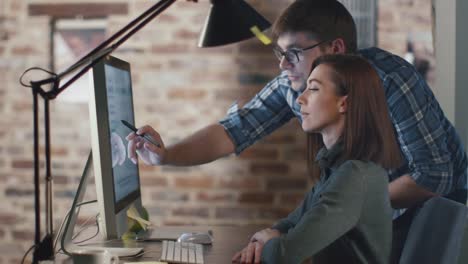 Young-man-and-woman-are-working-on-a-computer-in-a-loft-while-discussing-a-project.