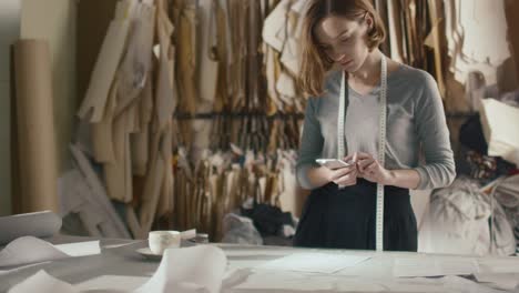 Female-clothing-designer-is-photographing-sewing-patterns-with-a-smartphone-on-a-studio-table.