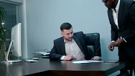 Afro-american-businessmen-counting-money-on-desk-and-giving-bills-to-his-caucasian-partner,-they-shaking-hands-positively