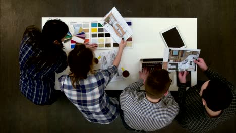 Two-architects-discussing-layout-while-female-coworkers-looking-at-color-palette