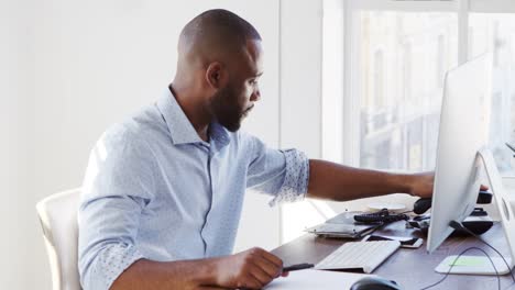 Young-black-man-using-phone-and-computer-in-office,-close-up