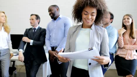 Afrikanische-amerikanische-Geschäftsfrau-halten-lächelnd-über-Menschen-Unternehmensgruppe-Brainstorming-Sitzung-im-modernen-Open-Office-Dokumente