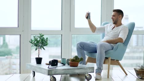 Young-happy-man-have-online-video-conference-using-digital-tablet-computer-sitting-on-balcony-in-modern-loft-office