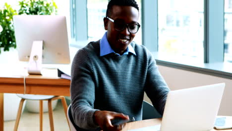 Male-executive-using-laptop-while-talking-on-mobile-phone