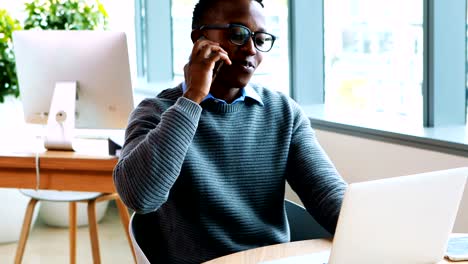 Male-executive-using-laptop-while-talking-on-mobile-phone