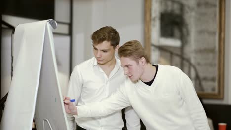 Two-guys-talks-near-flipchart-and-writes-something-on-it