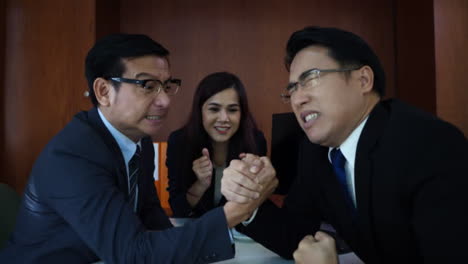 Business-people-arm-wrestling-at-desk-in-the-office