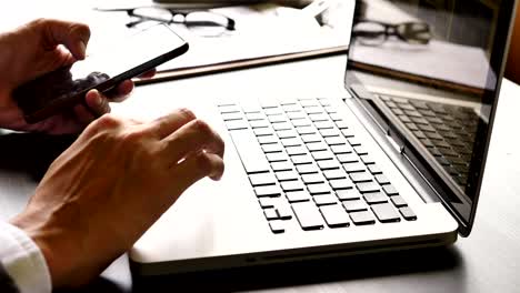 Close-up-of-businessman-using-laptop-and-smartphone-on-the-office-desk.